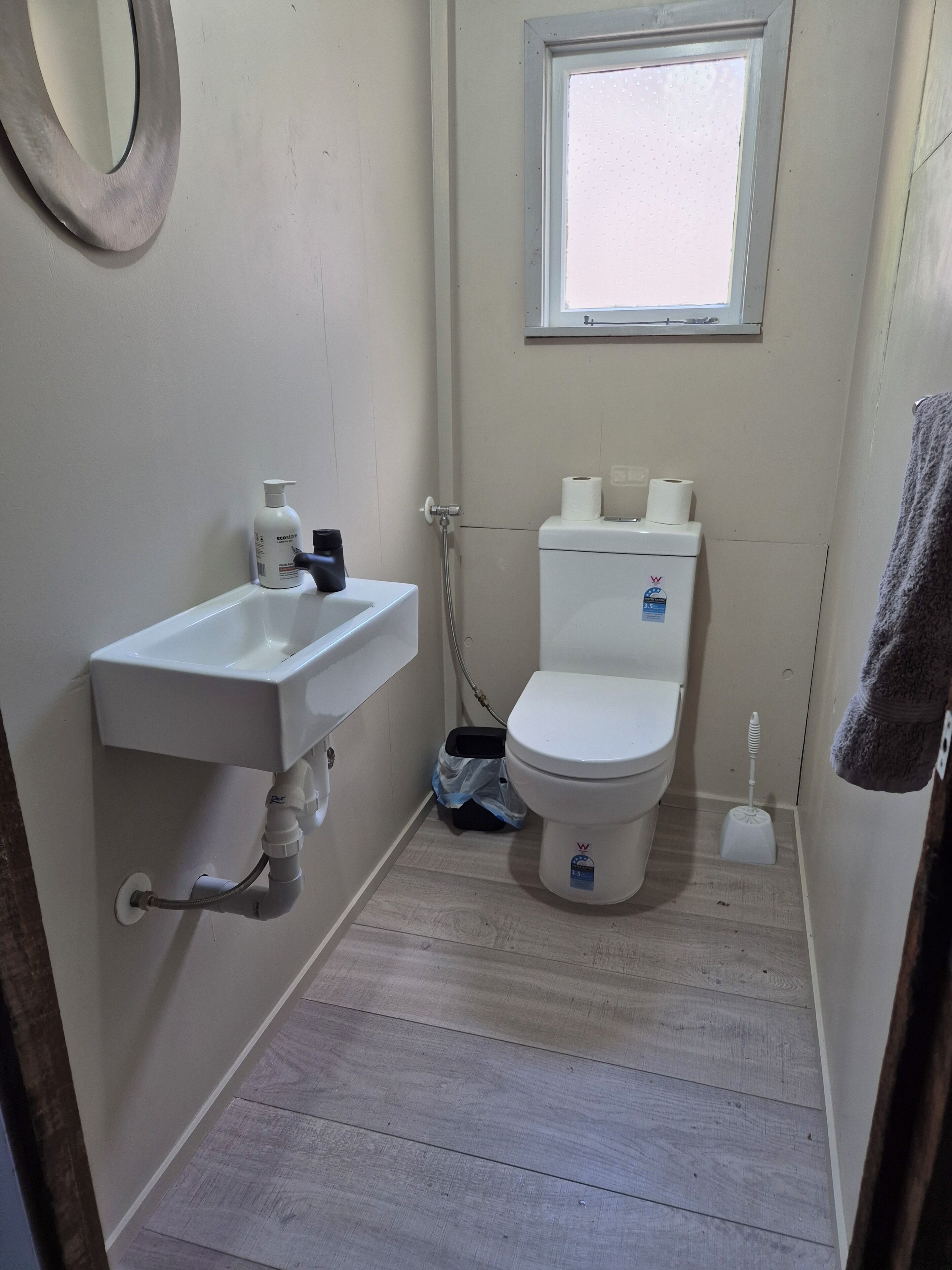 A small, compact bathroom with a white sink, toilet, and a window above the toilet.