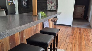A modern kitchen with a wooden bar counter, black stools, and a herringbone-patterned floor.