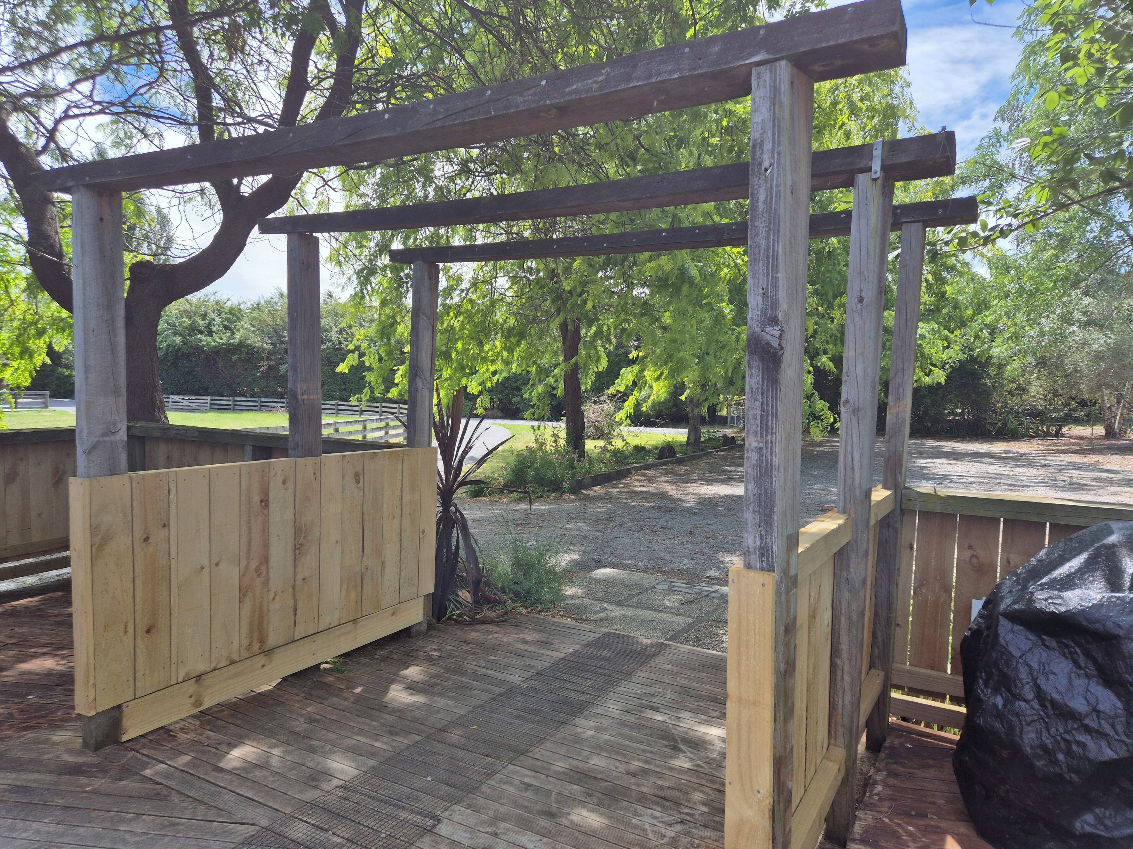Une structure de pergola en bois, avec un chemin de gravier en dessous.