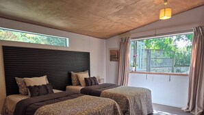 A bedroom with two beds, a wooden ceiling, a window with curtains, and a small potted plant.