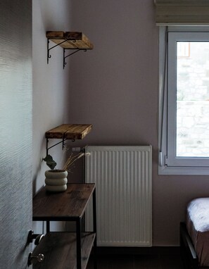 Une petite pièce faiblement éclairée, avec une table en bois, un radiateur et une fenêtre donnant sur un mur de pierre.