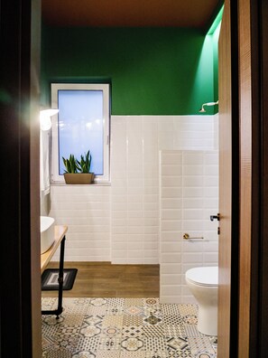 Une salle de bain avec des toilettes blanches, un lavabo, une fenêtre avec une plante et un mur vert.