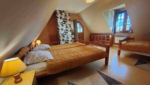 A bedroom with a sloped ceiling, two beds, a wooden nightstand, a lamp, and a patterned rug. - Farm cottage in a quiet location near the sea (Beaufour-Druval)