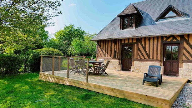 A wooden deck with outdoor furniture, a stone wall, and a house with a steeply pitched roof and exposed timber framing. - Farm cottage in a quiet location near the sea (Beaufour-Druval)
