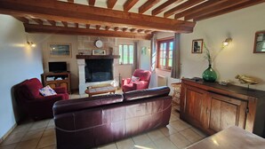 A cozy living room with a fireplace, leather sofa, wooden beams, and a dining area. - Farm cottage in a quiet location near the sea (Beaufour-Druval)