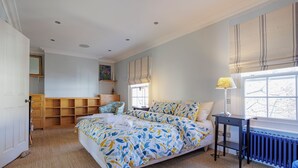 Une chambre à coucher comprenant un lit, une table de chevet, une lampe, une fenêtre avec des stores, un radiateur et une étagère intégrée.
