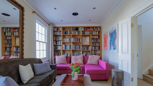 Un salon avec une grande bibliothèque, un canapé rose et une table basse en bois sur laquelle est posé un vase de fleurs.