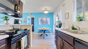 A modern kitchen with a toaster, stove, and sink. There is a dining table with blue chairs and a ceiling light. - Designer Resort Style - 1 King Bed Apartment, Pool, Gym in beautiful Gilbert AZ (Gilbert)