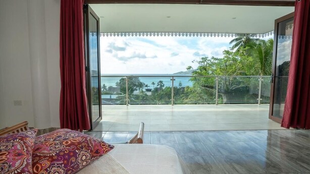 A room with a bed, a view of the sea, and a balcony with red curtains. - LA BELLE RESIDENCE (Mahe Island)