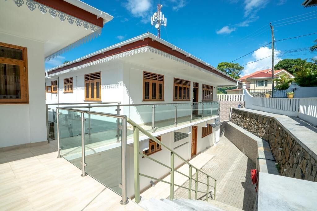 Une maison à deux étages avec un balcon, un mur en pierre et un ciel d’un bleu éclatant.