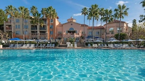 Ein Hotel mit großem Pool, Palmen und einem Gebäude im mediterranen Stil.