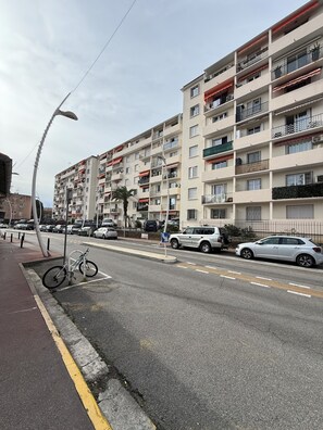 Ein mehrstöckiges Wohnhaus mit Balkonen, eine Straße mit geparkten Autos und ein Fahrrad auf dem Bürgersteig.