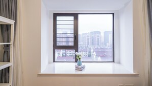 Una habitación con un amplio ventanal, un estante blanco y un jarrón con flores.
