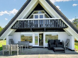 A two-story house with a balcony, a patio with outdoor furniture, and large windows. - 4 Star Holiday Home in Hojby (Hojby)