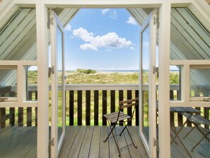 A wooden deck with a folding chair, a table, and a view of the beach and dunes. - 4 Star Holiday Home in Hojby (Hojby)