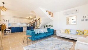 Ein großzügiger Wohnbereich mit einem blauen Sofa, einem weißen Sofa und einem Marmorbildteppich. Im Hintergrund ist eine Küche mit weißen Schränken und einer blauen Arbeitsplatte zu sehen.