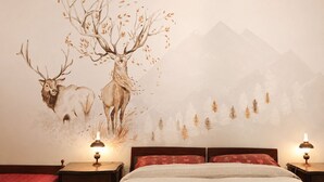 Ein Schlafzimmer mit einem Bett, zwei Nachttischen mit Lampen und einem Wandbild von Hirschen und Bäumen.