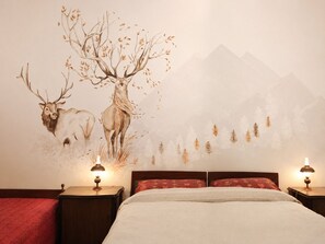 Un dormitorio con una cama, dos mesitas de noche con lámparas y un mural en la pared con ciervos y árboles.