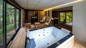 Ein Zimmer mit einer großen Badewanne, Korbmöbeln und Blick auf den Wald.