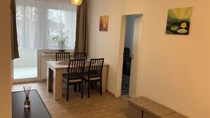 A dining area with a table and chairs, a hanging light fixture, a window with sheer curtains, and a door leading to another room. - At Biebrich Palace Park (Wiesbaden)