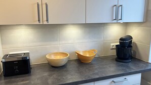 A kitchen with white cabinets, a toaster, a wooden bowl, and a coffee maker on the countertop. - At Biebrich Palace Park (Wiesbaden)