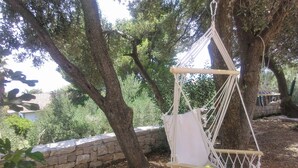 A hammock chair suspended from a tree, surrounded by greenery and a stone wall.