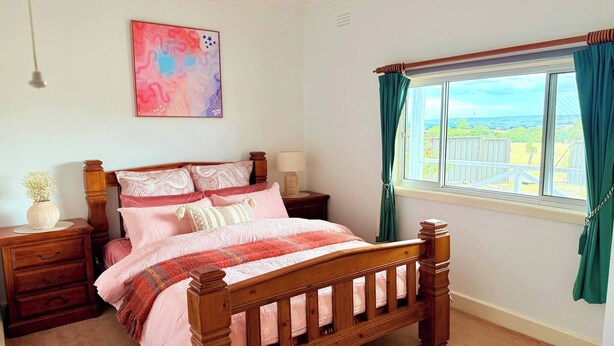 A bedroom with a wooden bed, a nightstand, a bedside table, a lamp, a window with curtains, and a wall art piece. - Quiet Farm-style Retreat With Scenic Views (Durham Lead)