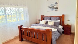 A bedroom with a wooden bed, a nightstand, a framed picture on the wall, and a window with a white curtain. - Quiet Farm-style Retreat With Scenic Views (Durham Lead)