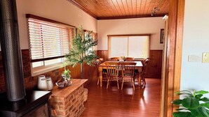 A cozy dining area with wooden furniture, a brick fireplace, and large windows with blinds. - Quiet Farm-style Retreat With Scenic Views (Durham Lead)