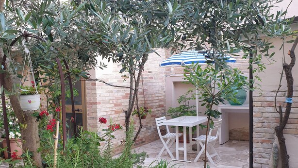 A patio area with a table and chairs, surrounded by potted plants and a brick wall. - 60sqm downtown with garden | Casa Da Diego (Civitanova Marche)