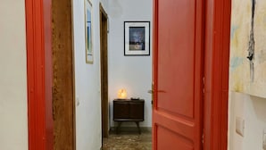 A hallway with a red door, a wooden door frame, a small cabinet with a lit lamp, and a framed picture on the wall. - 60sqm downtown with garden | Casa Da Diego (Civitanova Marche)