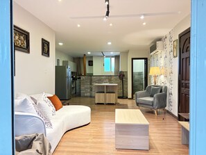 A modern living room with a sofa, a coffee table, and a dining area with a table and chairs. There is a kitchen in the background with a refrigerator and a window. - Soma-Rooftop Maadi (Cairo Governorate)