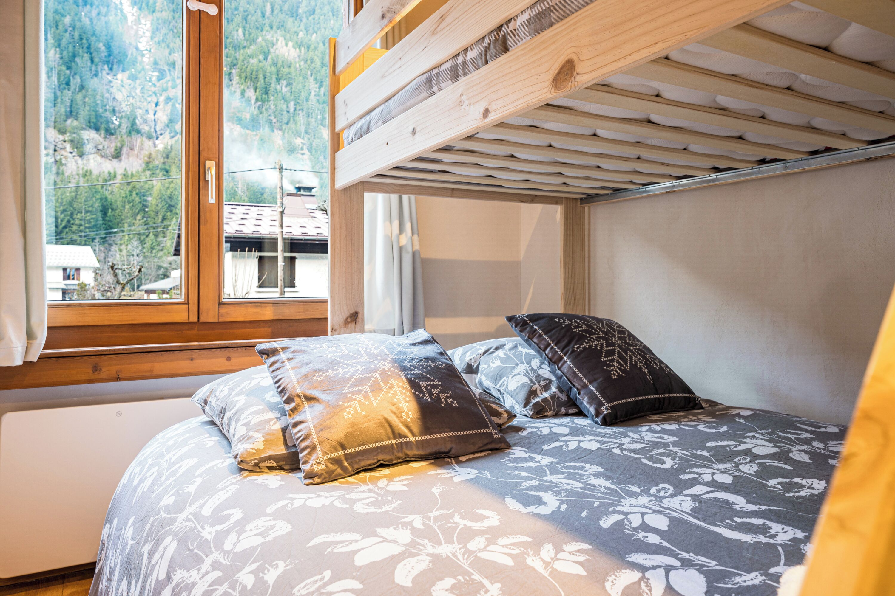 Une chambre avec un lit superposé, une fenêtre donnant sur une montagne et un lit avec une literie à motifs.