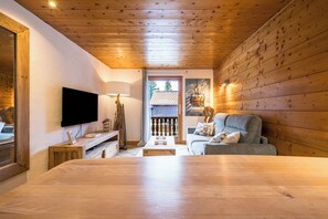 A cozy room with a wooden ceiling, a flat-screen TV mounted on the wall, a grey sofa with cushions, and a wooden table in the center. - Argentière 7p facing Aiguille du Midi Close to pistes (Chamonix-Mont-Blanc)