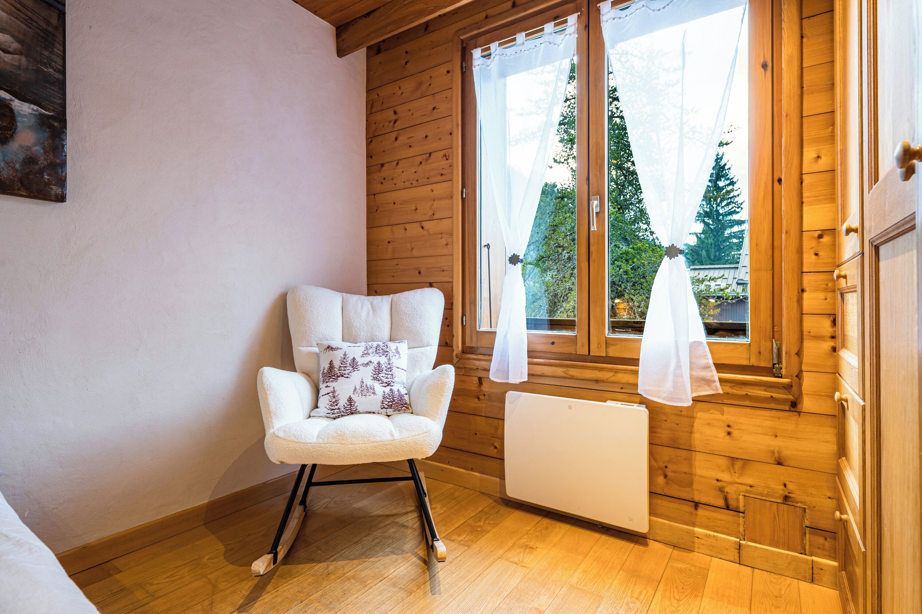 Une pièce chaleureuse aux murs en bois, avec un radiateur blanc et un fauteuil à bascule doté d’un coussin.