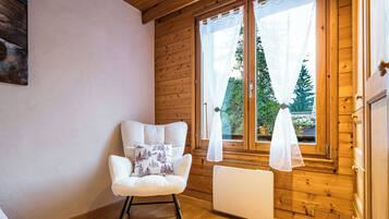 Une pièce chaleureuse aux murs en bois, avec un radiateur blanc et un fauteuil à bascule doté d’un coussin.