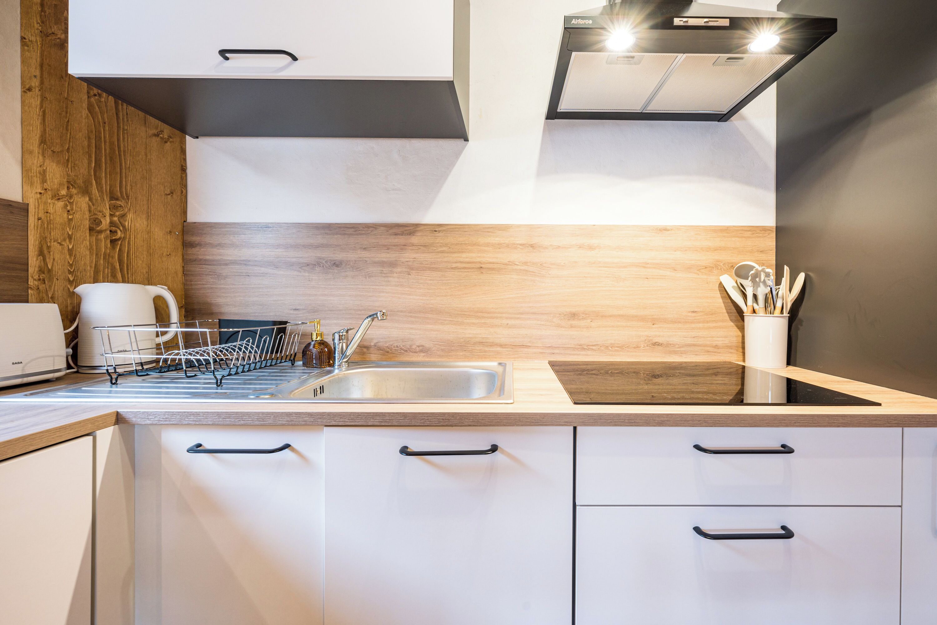 A modern kitchen with a stainless steel sink, white cabinets, and a wooden backsplash.