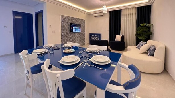 A modern dining area with a blue table and white chairs, a black sofa, and a large plant.