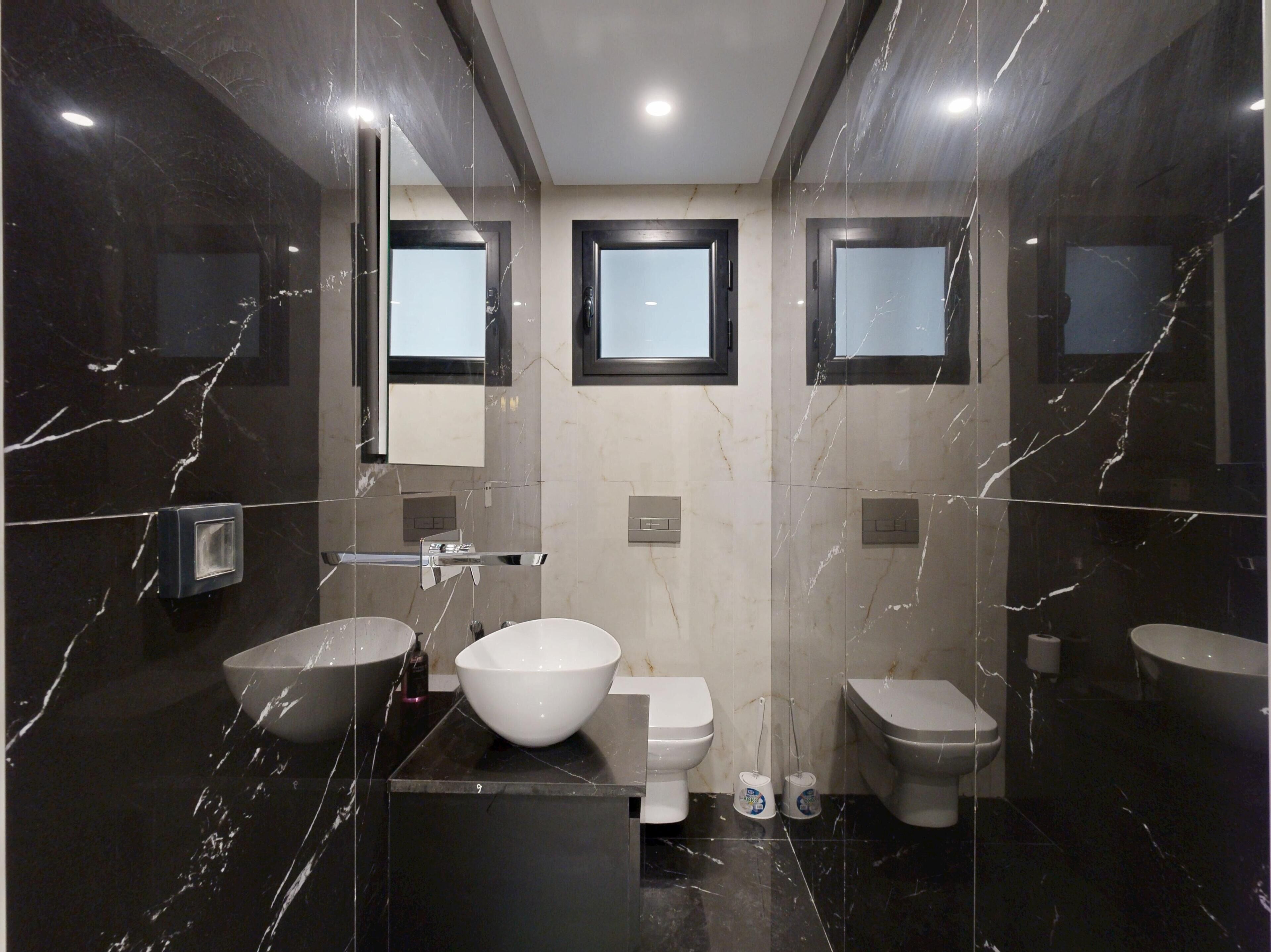 A modern bathroom with a large mirror, two sinks, a toilet, and a bidet.