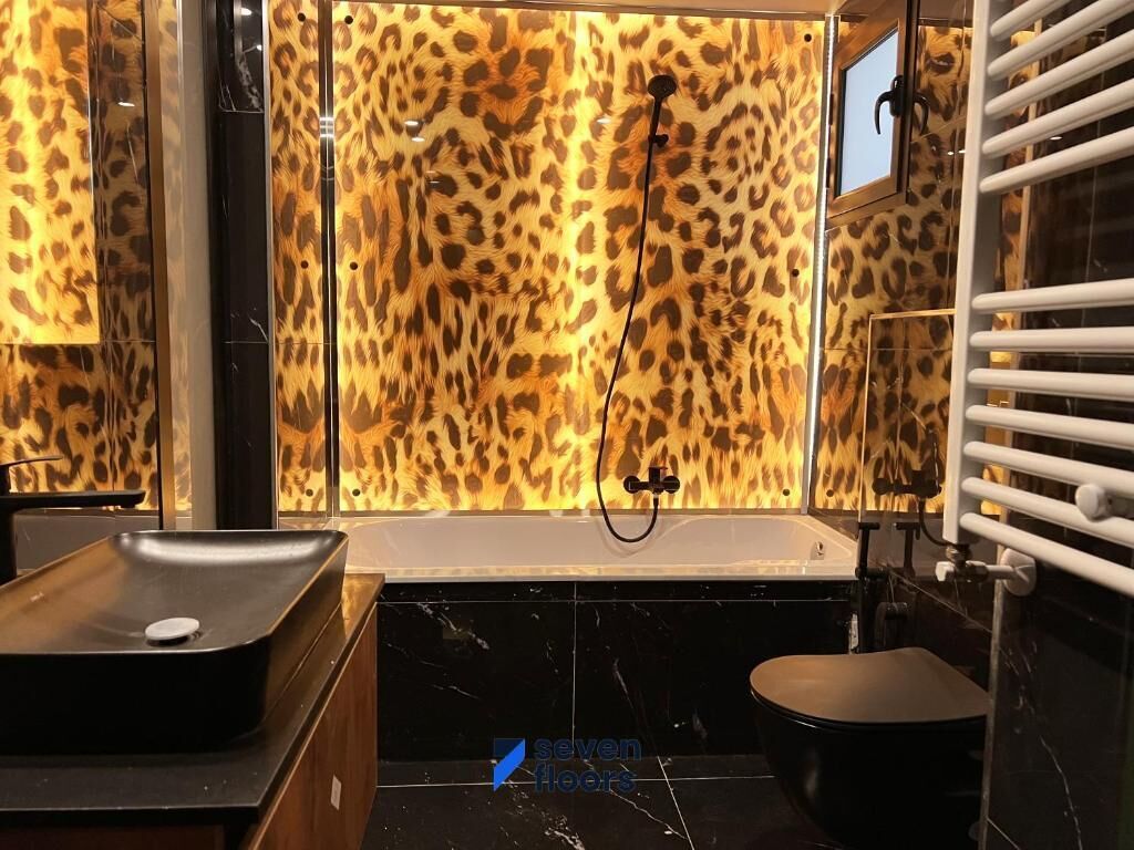 Un baño con cabina de ducha de estampado de leopardo, un lavamanos negro y una bañera blanca.