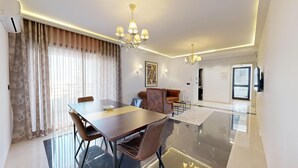A modern living room with a dining area, a chandelier, and a large window with curtains.