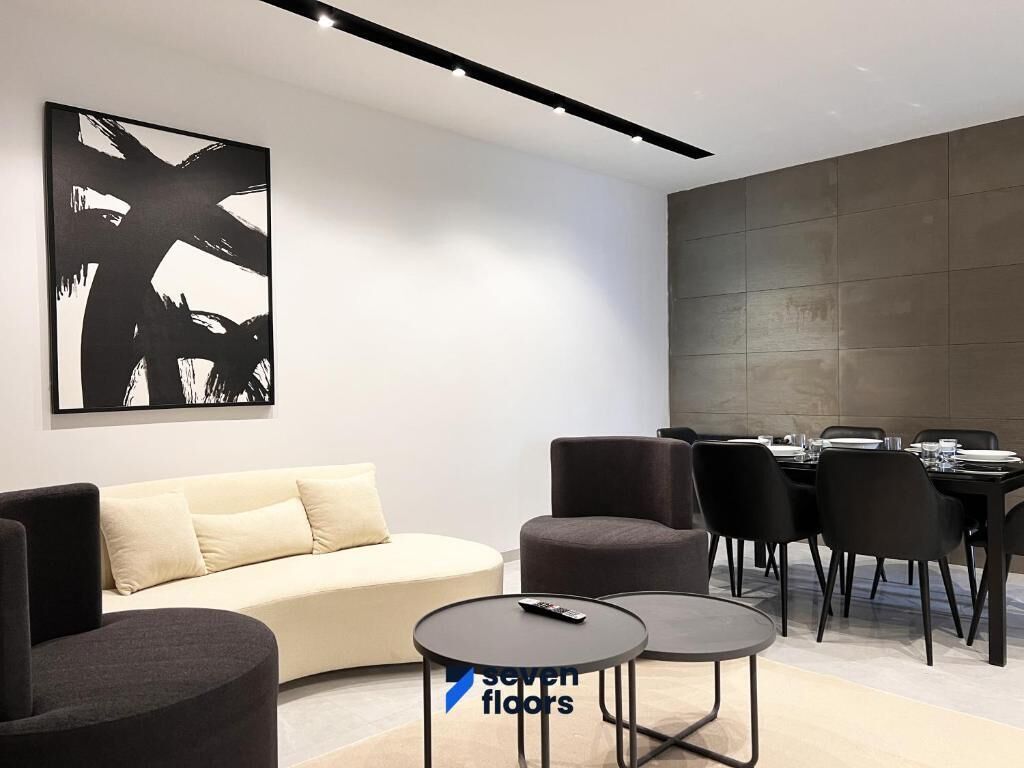 A modern interior with a sofa, two round tables, and a dining area with chairs.