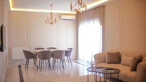 A modern living room with a sofa, a dining table with chairs, and a chandelier.