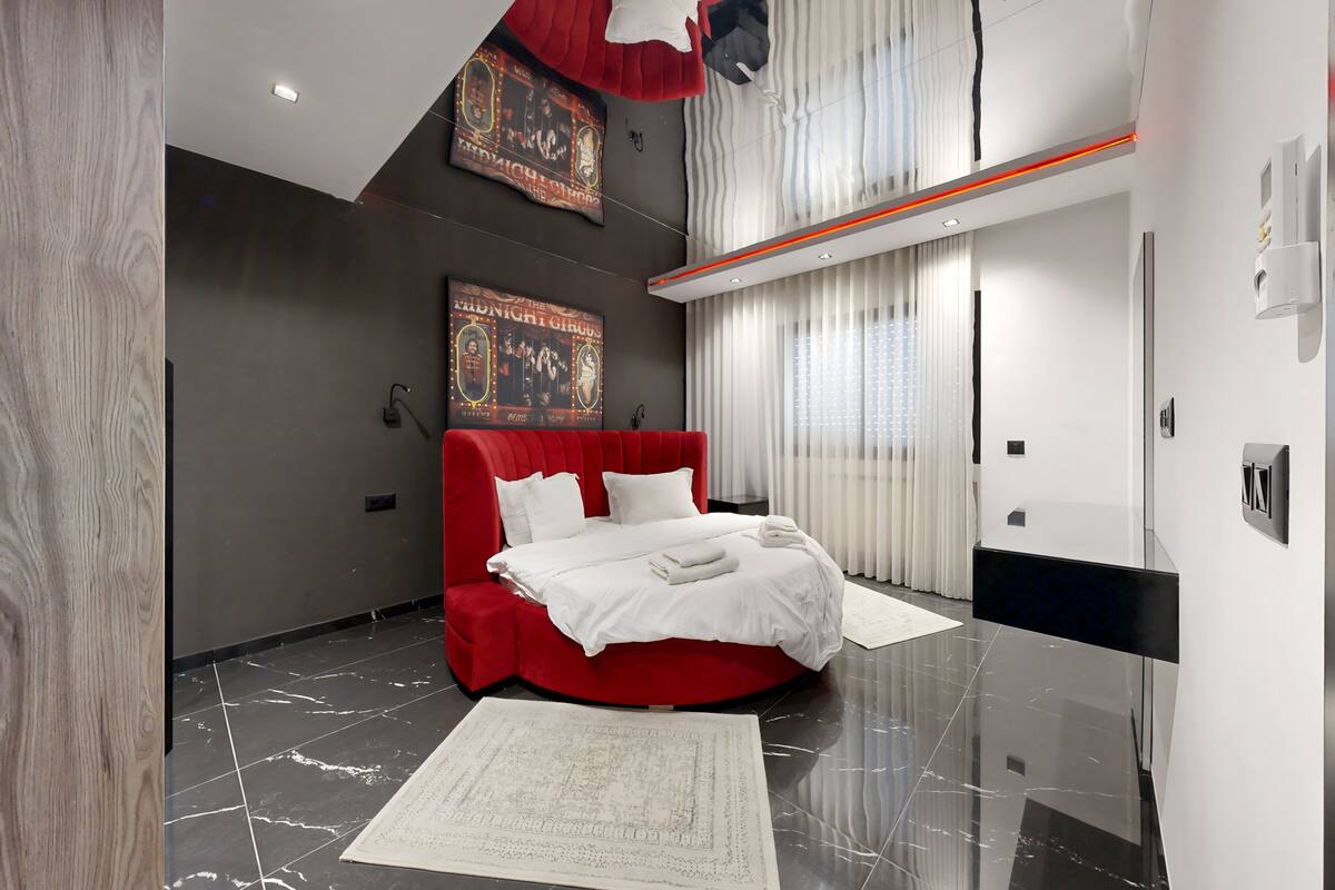 Una habitación de hotel moderna con una cama tapizada en rojo, un cartel grande en la pared y un suelo de mármol.