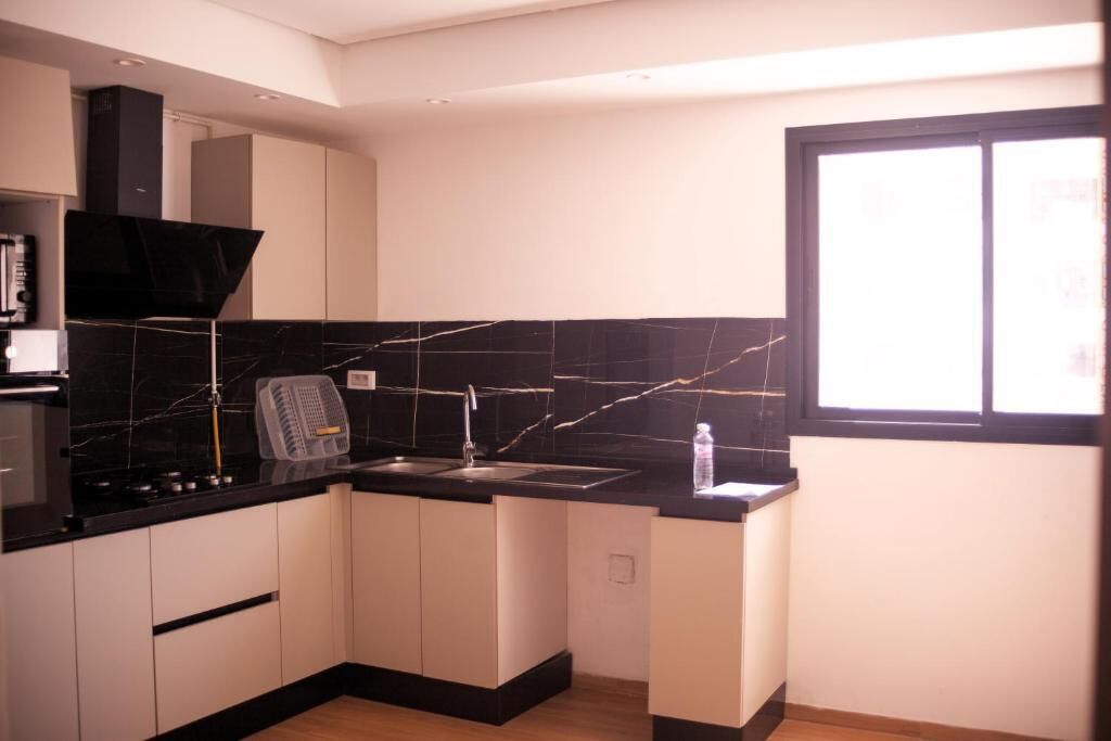 Cocina compacta con salpicadero de mármol negro, armarios blancos y ventana que proporciona luz natural.