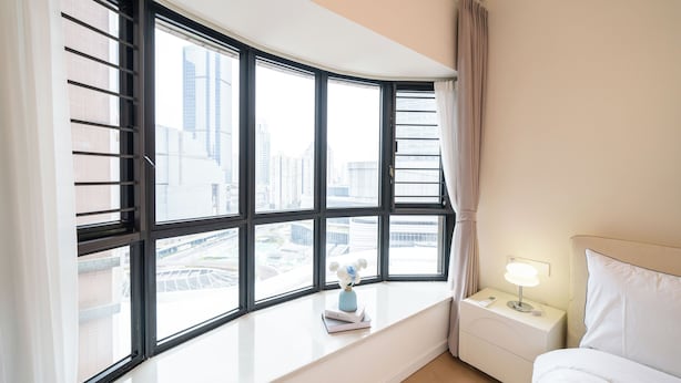 A hotel room with a curved window, a bedside table with a lamp, and a bed. - Tyms 3BR 2BA Apt  Gubei Fully Furnished (Shanghai)