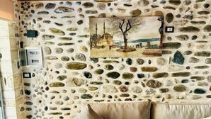 Una habitación con pared de piedra, techo de madera, sofá color crema y lámpara colgante.
