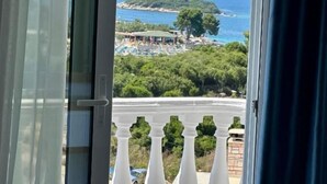 Un balcón con vista a una playa, una pequeña isla y una cadena montañosa.