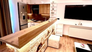 Una cocina moderna con una isla de madera, armarios blancos, una estufa integrada y un televisor de pantalla plana montado en la pared.