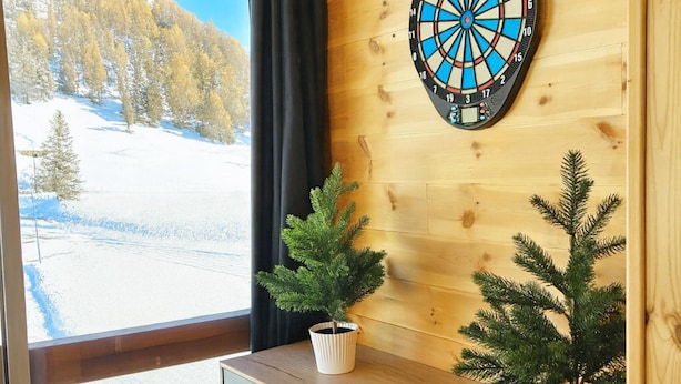 Quarto com parede de madeira, um alvo de dardos e duas plantas em vasos.